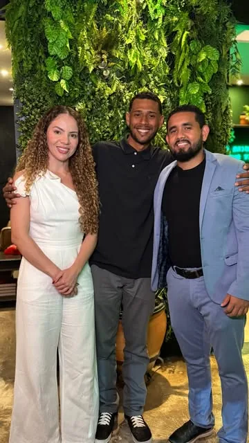 Três pessoas sorrindo num evento, diante de uma parede de plantas