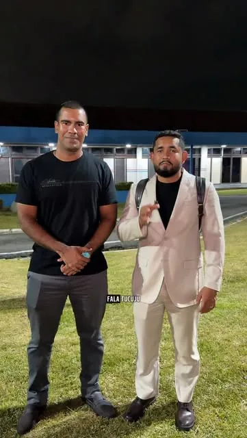 Dois homens lado a lado num gramado, à noite